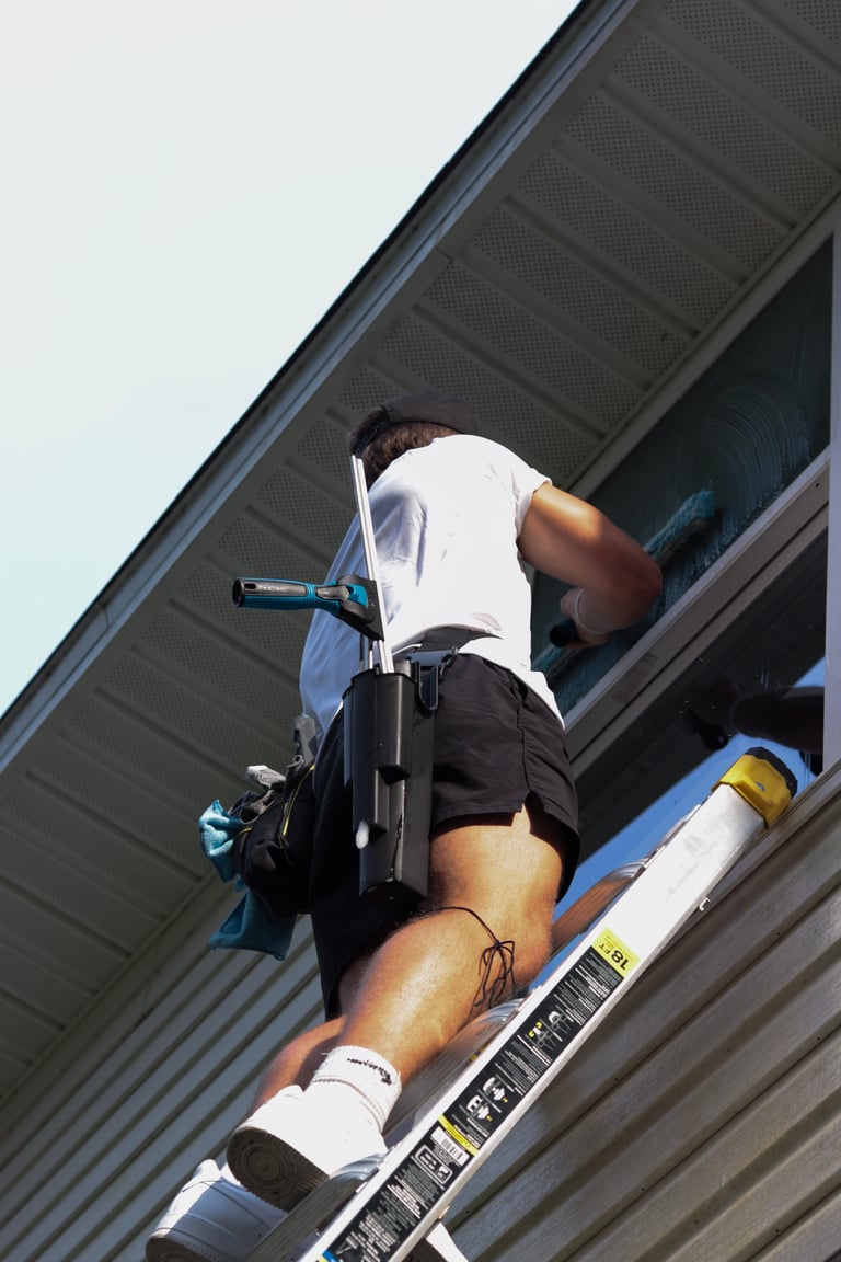 Worker on a ladder installing or repairing a gutter on a residential building roof under a clear blue sky