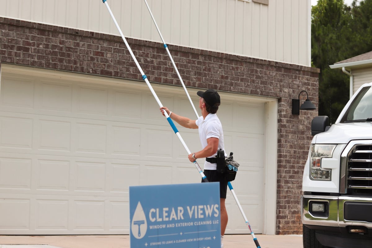 Clear Views technician using an extended pole to clean second-story windows on a brick home