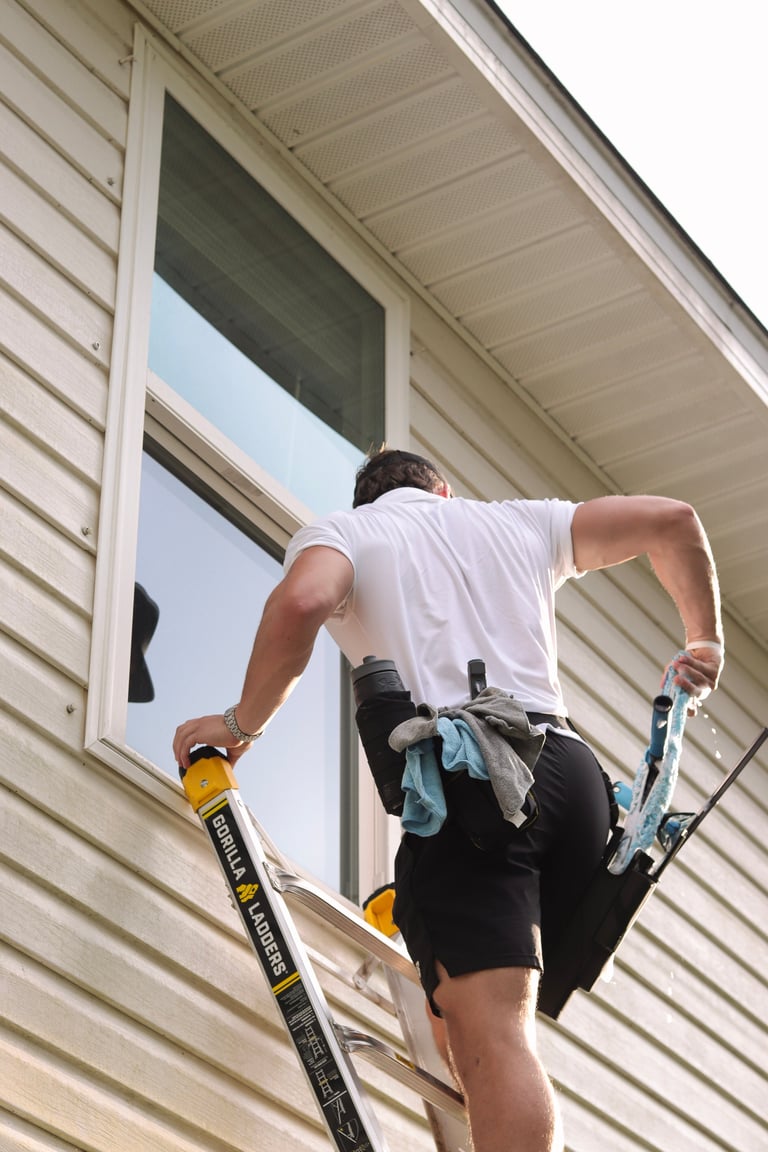 Man on ladder cleaning or installing a window on a house with beige vinyl siding