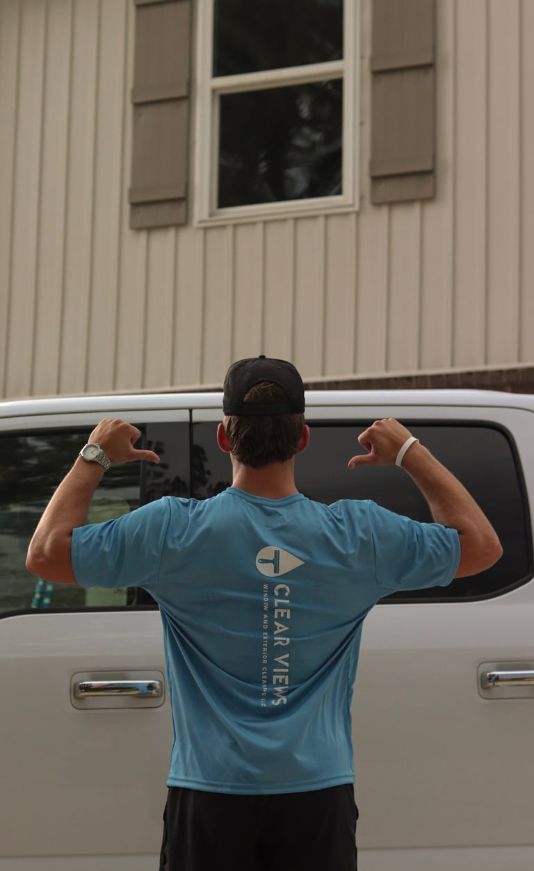 Person in blue shirt flexing arms while standing in front of white van and building with window
