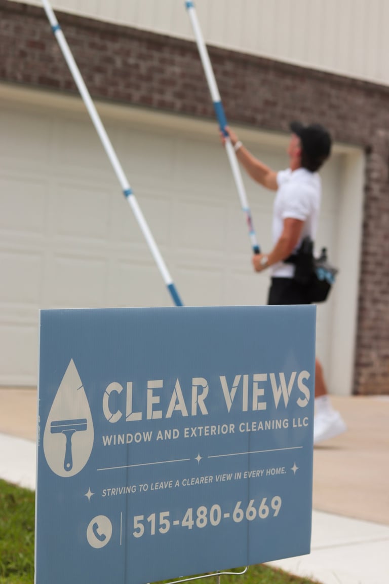 Clear Views Window and Exterior Cleaning LLC yard sign with worker cleaning upper building exterior with long-handled poles
