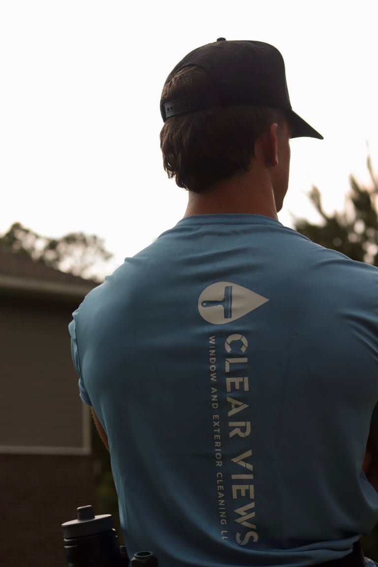 Man wearing blue Clear Views shirt and black cap viewed from behind, standing outdoors with blurred background
